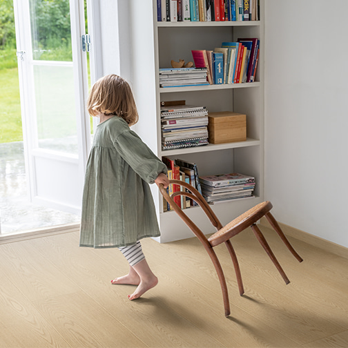 little girl dragging chair over beige laminate floor